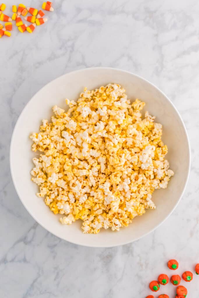 Large white bowl filled with freshly popped popcorn on a marble countertop with candy corn and pumpkins scattered around.