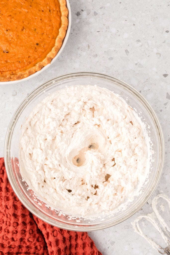 Fully mixed spiced whipped cream with visible flecks of cinnamon and nutmeg in a large bowl.