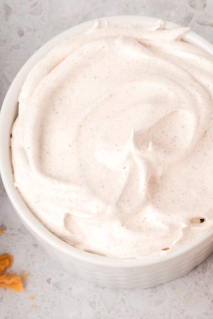Close-up of fluffy spiced whipped cream with specks of cinnamon in a white ramekin.