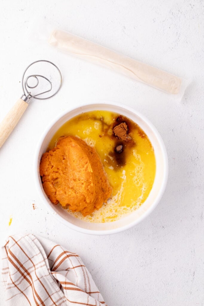 Mixing bowl filled with mashed sweet potatoes, melted butter, eggs, and spices before blending for sweet potato pie filling.