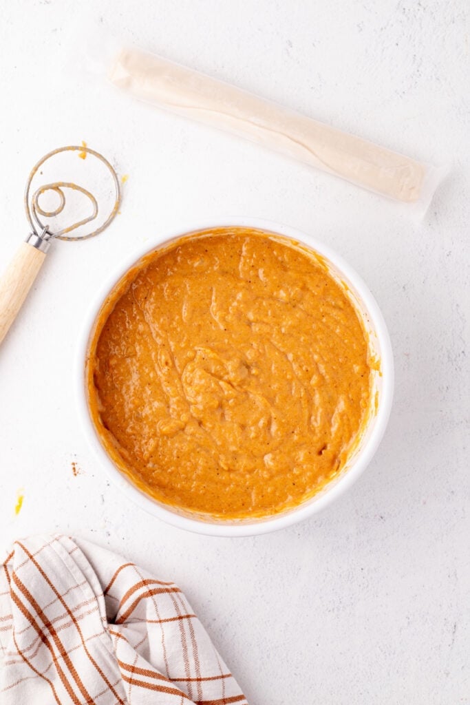 Smooth orange sweet potato pie filling in a white bowl after whisking ingredients together.