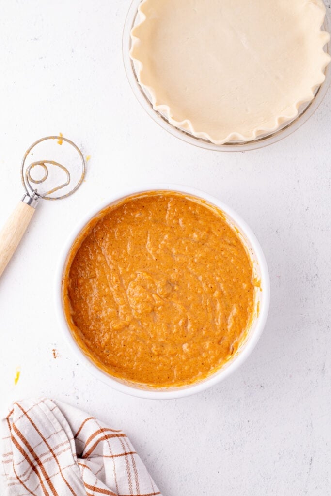 Sweet potato pie filling in a bowl next to an unbaked pie crust ready for assembly.