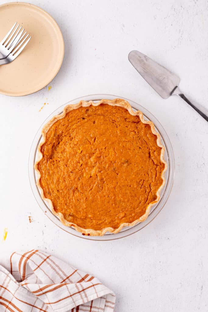 Fully baked sweet potato pie with a golden-brown crust cooling on a light background.