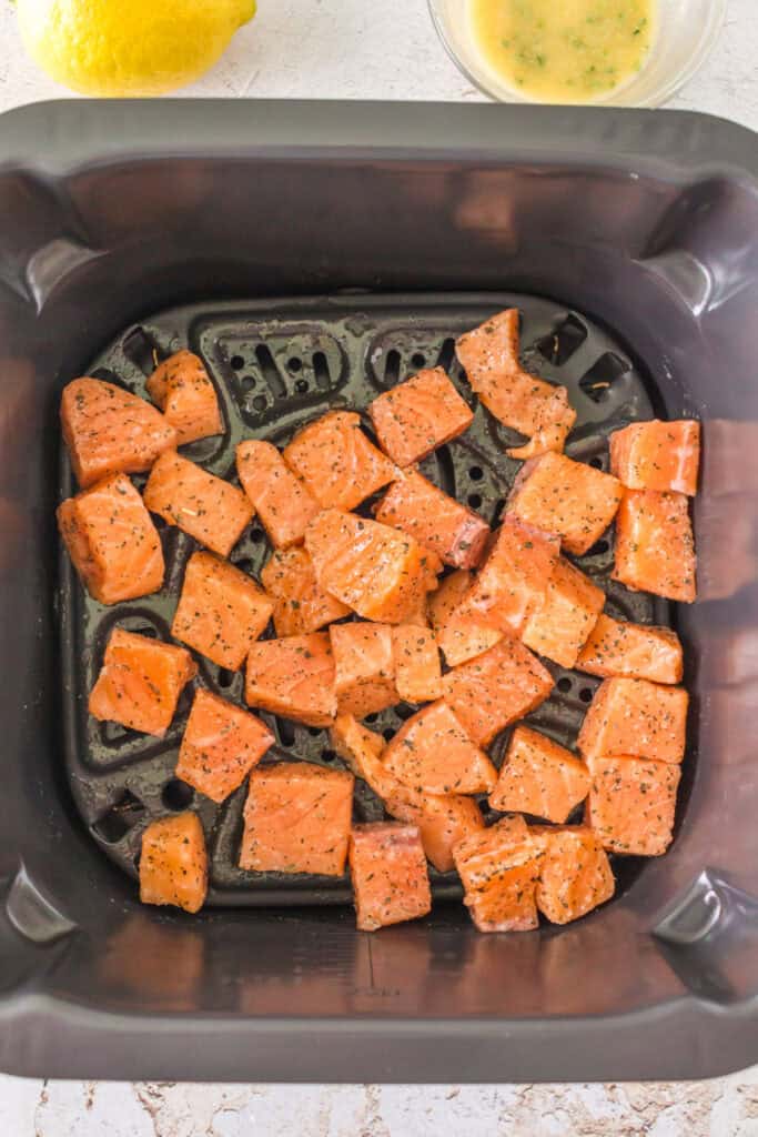 Seasoned salmon cubes arranged evenly in an air fryer basket, ready to cook.