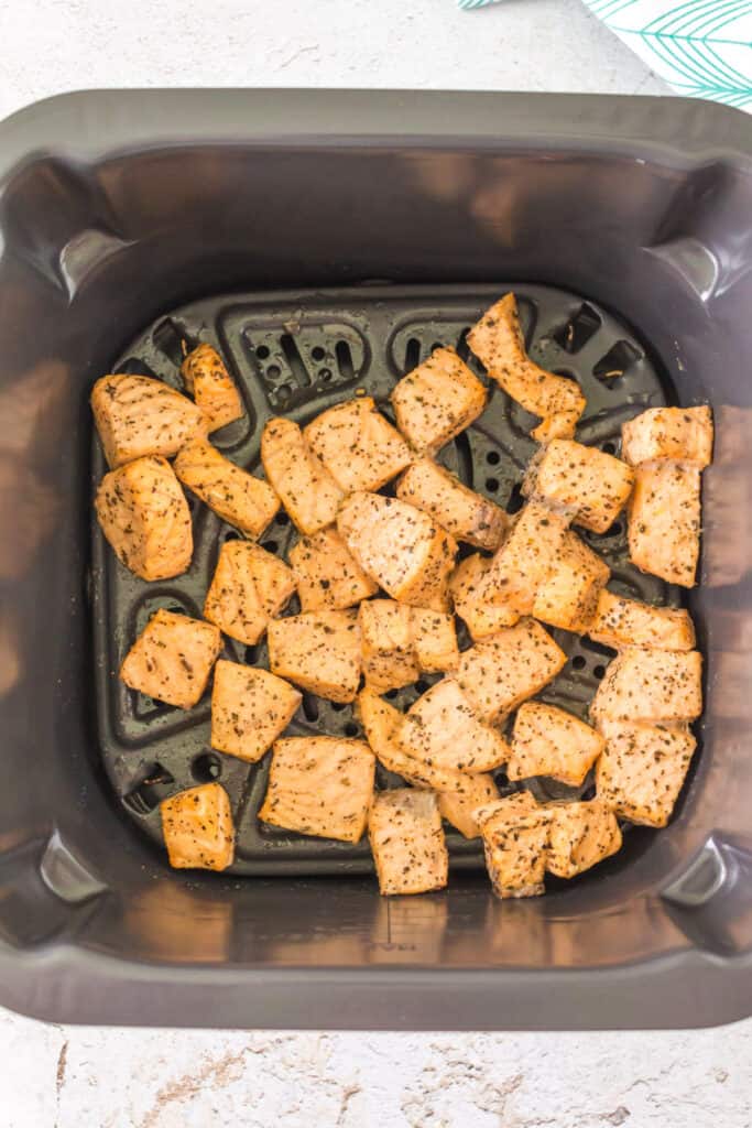 Cooked salmon bites in an air fryer basket showing golden color and crisp edges.
