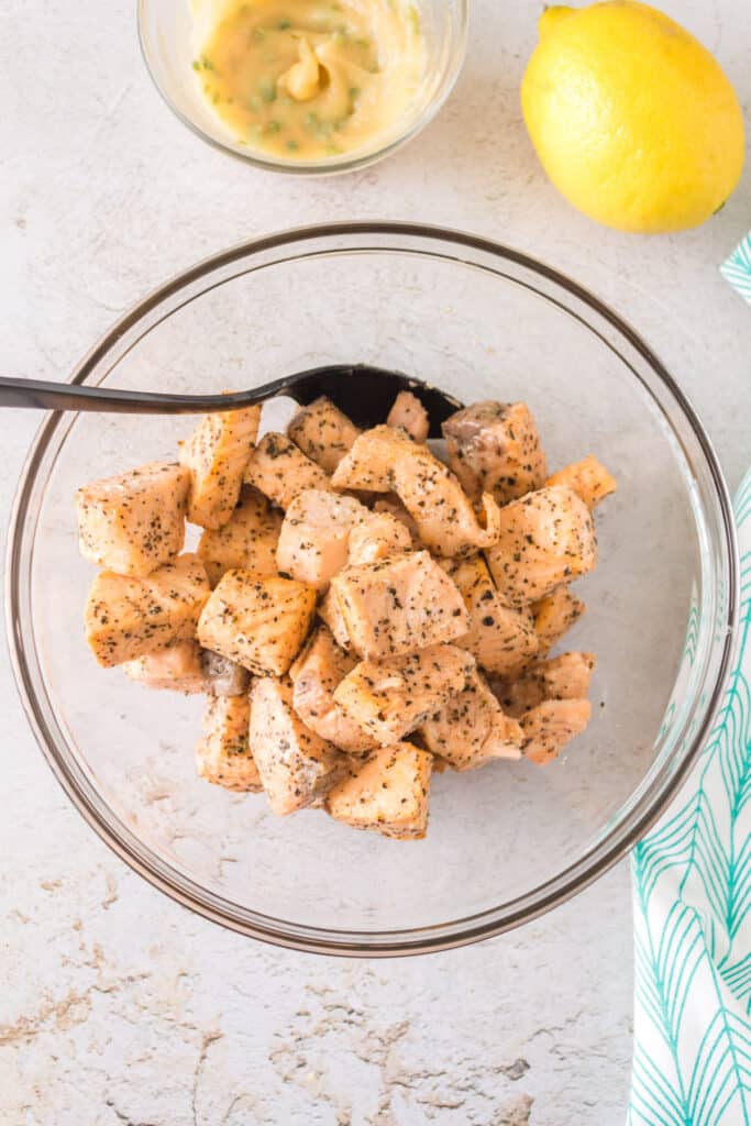 Bowl of freshly cooked salmon bites beside a lemon and bowl of garlic butter mixture.