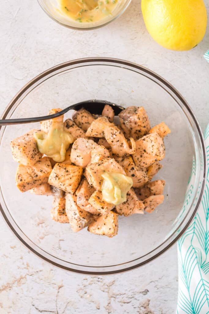 Salmon bites being drizzled with melted garlic butter in a clear mixing bowl.
