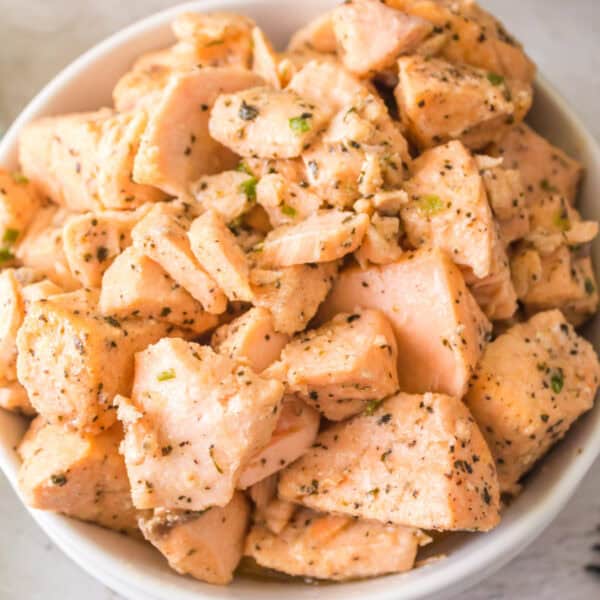 Close-up of a white bowl filled with tender, seasoned air fryer salmon bites coated in garlic butter and herbs.