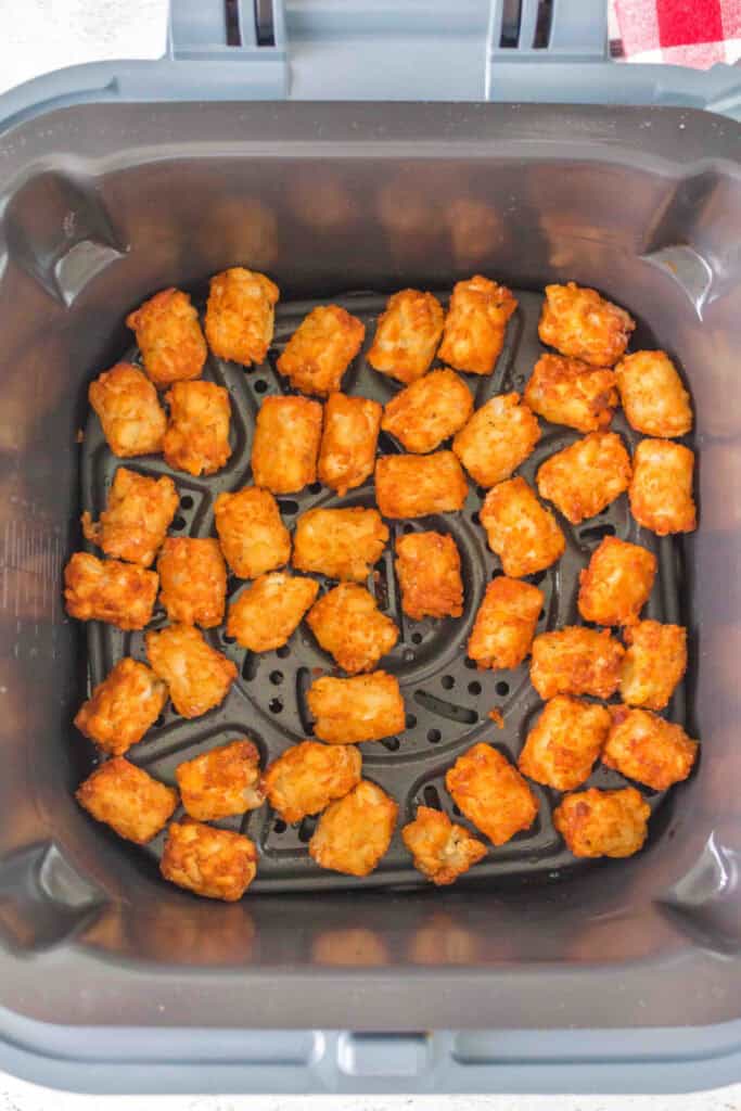 Golden brown tater tots in an air fryer basket after cooking until crisp.