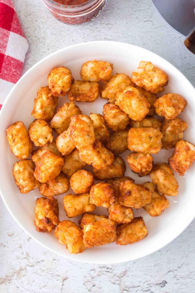 A white bowl filled with crispy cooked tater tots on a light textured surface.