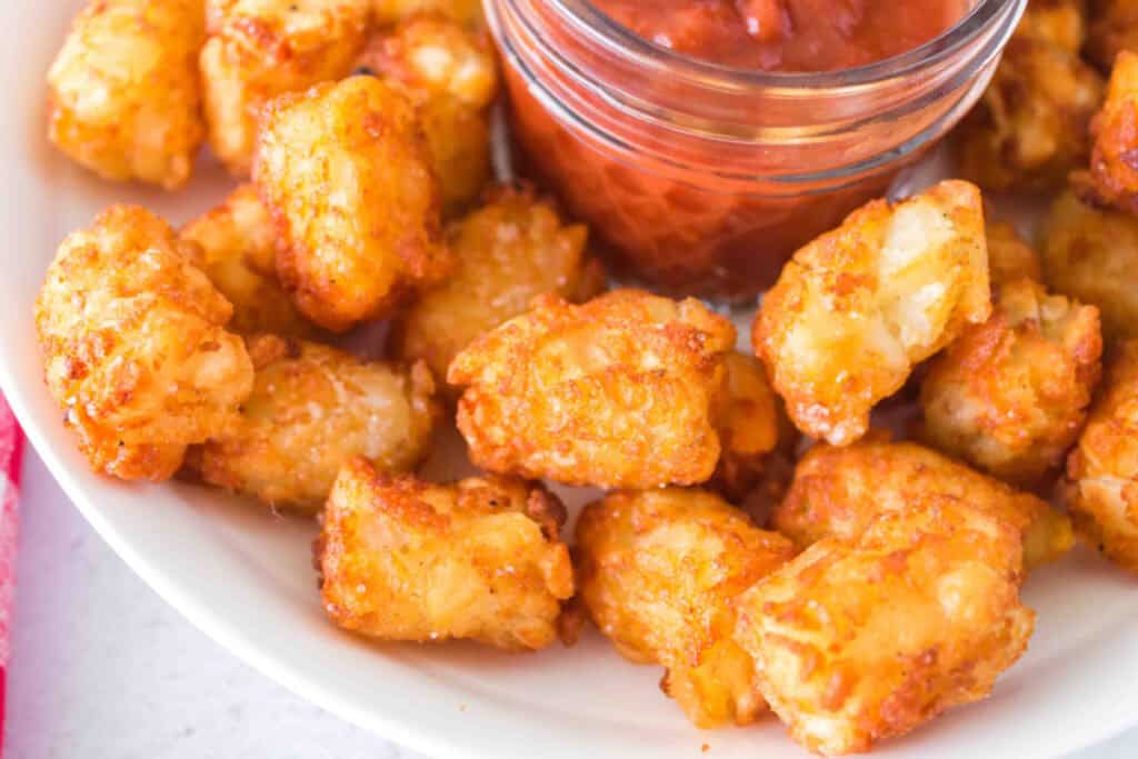 Close up view of crispy tater tots next to a small jar of ketchup for dipping.