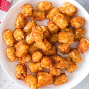 Crisp, golden tater tots piled in a white bowl on a light textured surface.