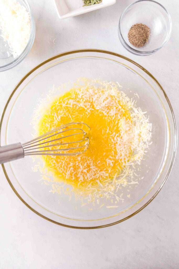 Egg yolks and grated cheese being whisked together in a clear mixing bowl.