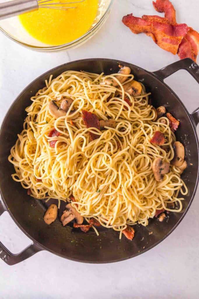 Spaghetti added to the skillet with cooked mushrooms and bacon before mixing.