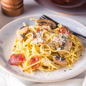 Square image of Bacon Mushroom Carbonara on a plate with mushrooms, bacon pieces, and fresh grated cheese on top.