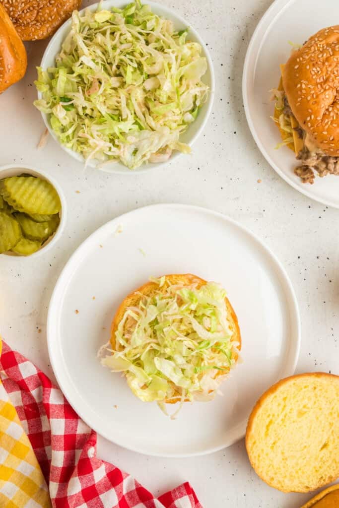 Bottom bun layered with lettuce, ready to assemble the Big Mac Sloppy Joes with the beef mixture and toppings.