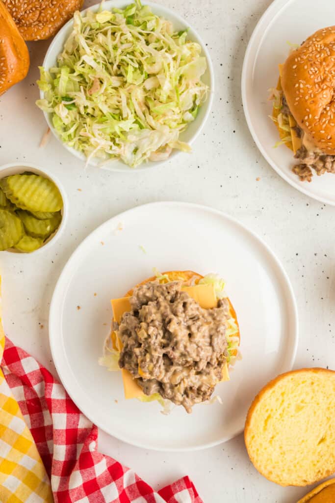Adding the cheesy beef mixture on top of lettuce and cheese during assembly of Big Mac Sloppy Joes.