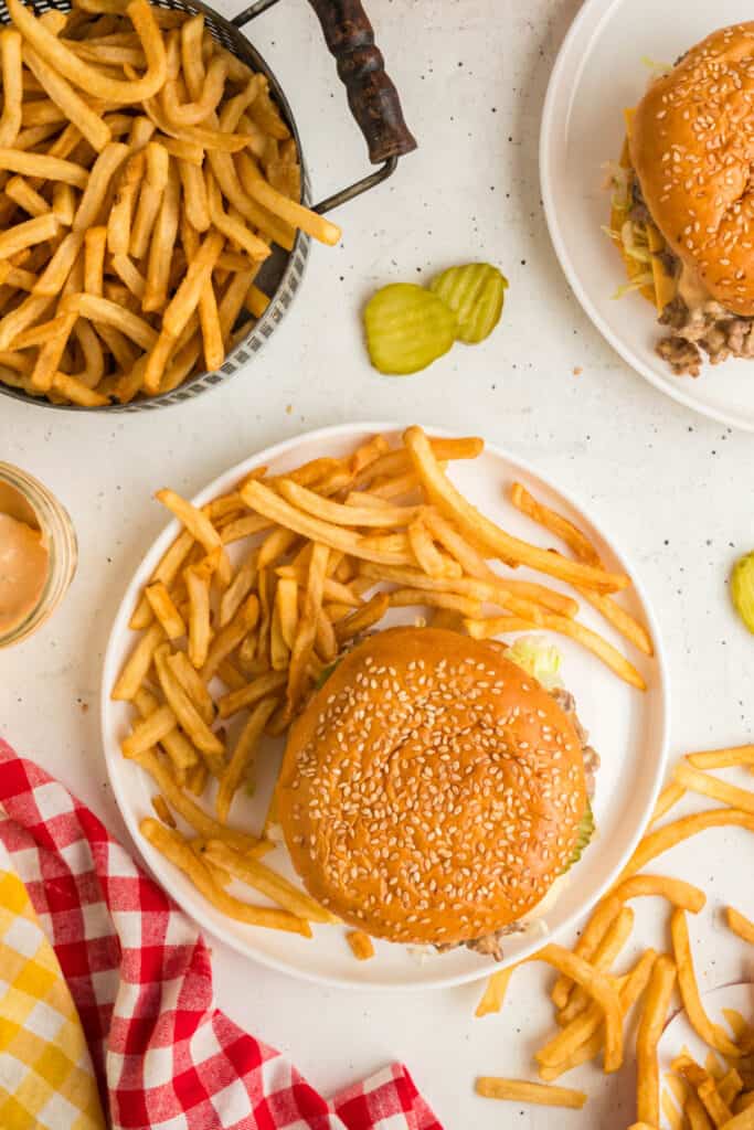 Overhead view of assembled Big Mac Sloppy Joes on a plate with golden fries and pickles on the side.