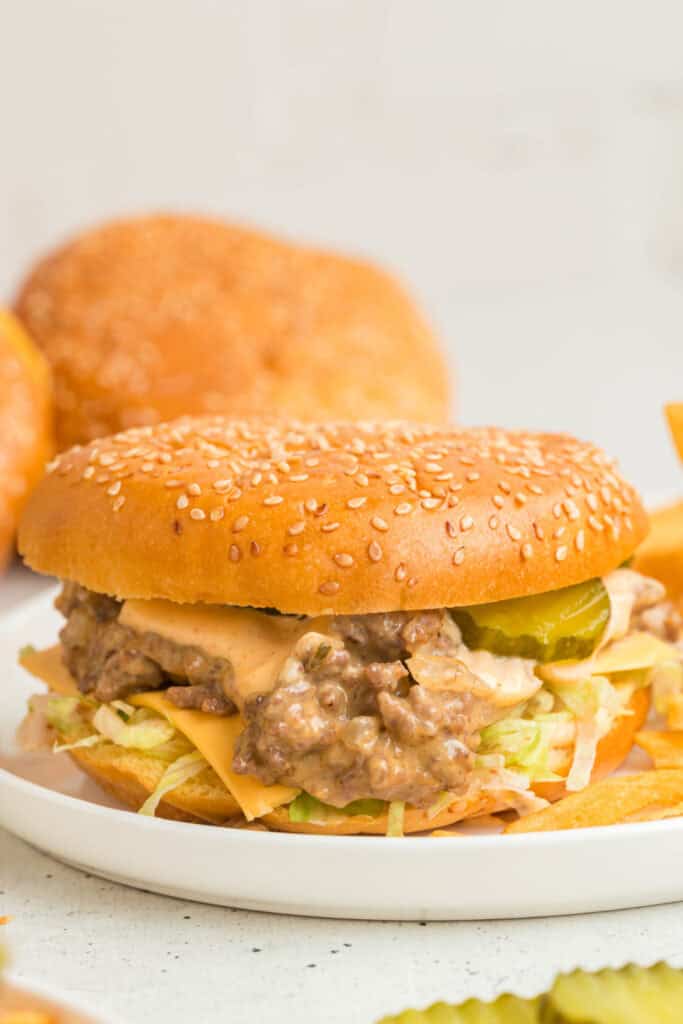 Close-up side view of Big Mac Sloppy Joes showing melted cheese, sauce, pickles, and lettuce on a sesame seed bun.