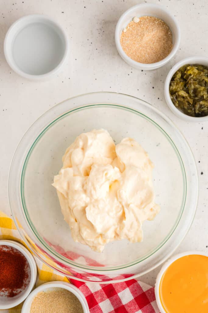 Bowl of mayonnaise surrounded by small bowls of relish, vinegar, garlic powder, paprika, and other Big Mac sauce ingredients on a white countertop.
