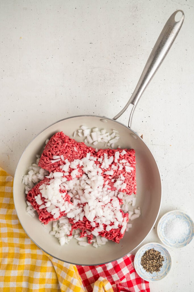 Skillet with raw ground beef and diced onions being cooked together for the Big Mac Sloppy Joes beef mixture.