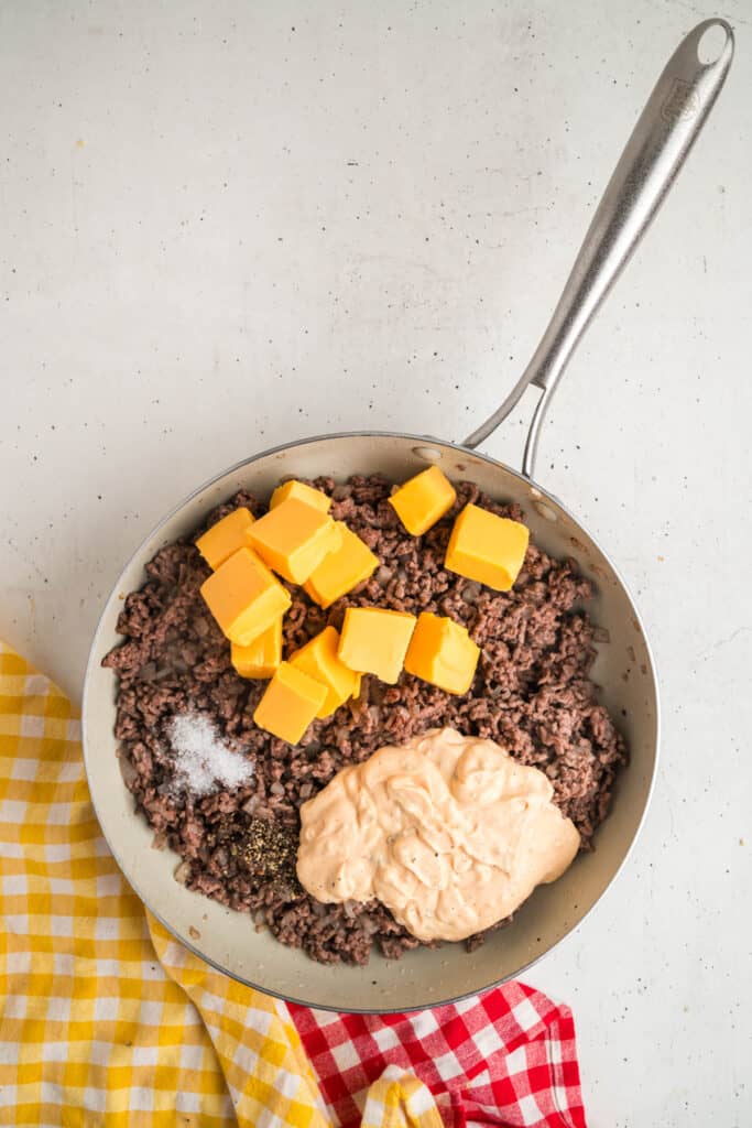 Skillet of cooked beef mixture with added Velveeta cheese cubes, seasoning, and Big Mac sauce before stirring.