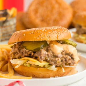 Square image of Big Mac Sloppy Joes with melted cheese, lettuce, pickles, and sauce on a sesame seed bun, served with fries.