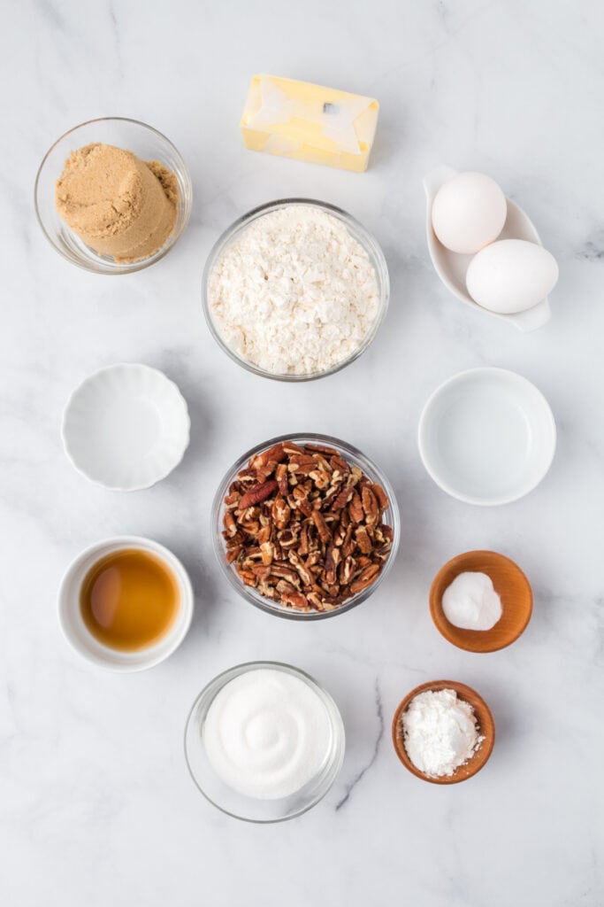 Overhead shot of butter, sugars, flour, pecans, eggs, and extracts measured out for making Butter Pecan Cookies on a marble surface.