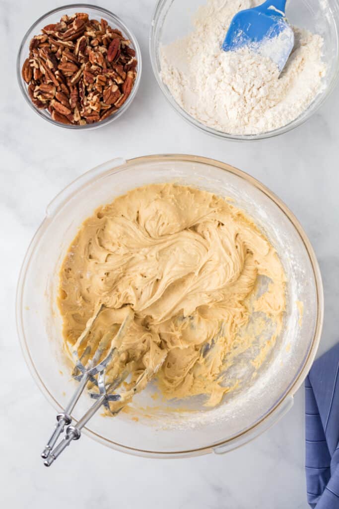Cookie dough mixed and ready in a glass bowl beside chopped pecans and dry ingredients for Butter Pecan Cookies.