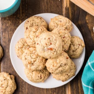 Overhead view of Butter Pecan Cookies piled on a white plate beside a turquoise napkin and mug of milk.