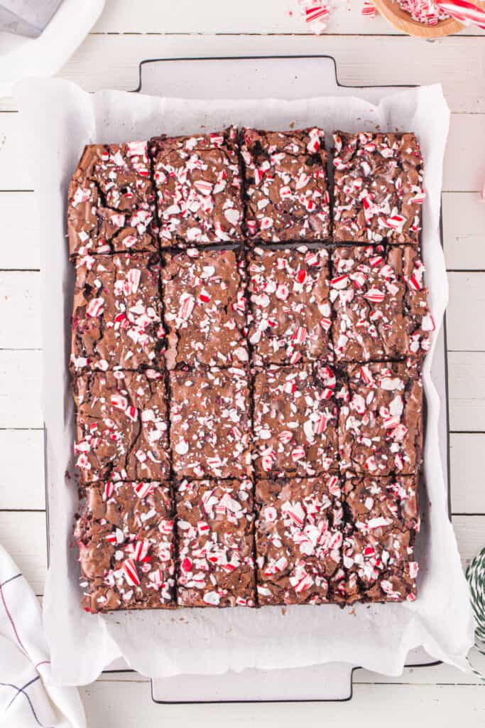 A full pan of sliced Candy Cane Brownies topped with crushed peppermint pieces, shown overhead on parchment paper.