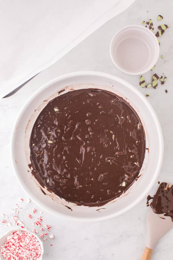 Brownie batter mixed with mint fudge baking chips in a white bowl, ready to be poured into the baking pan.