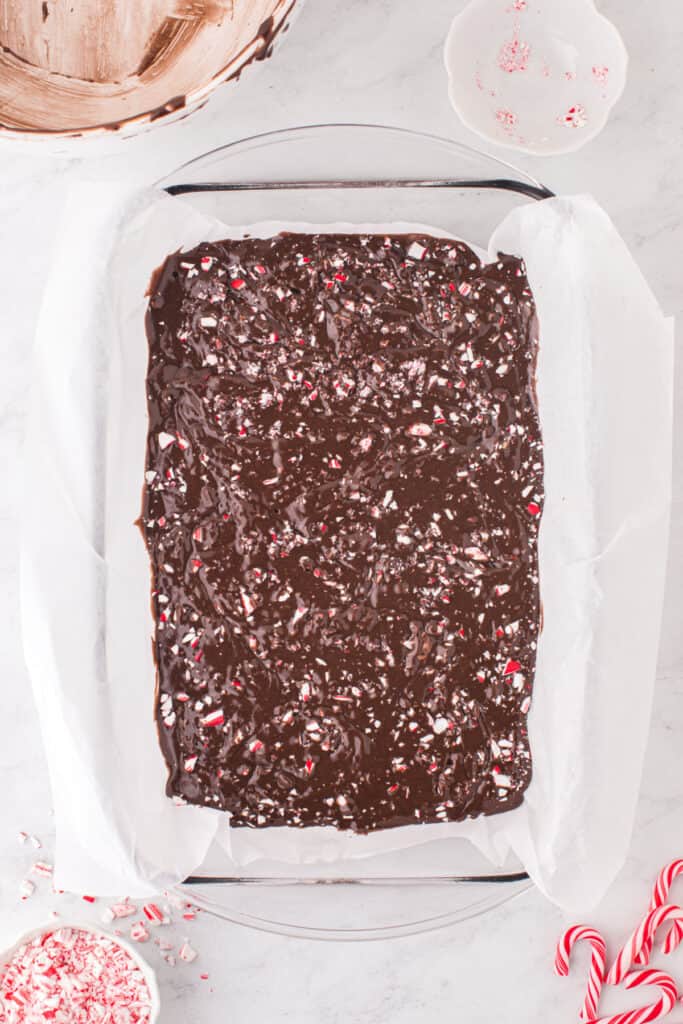 A close view of the raw brownie batter swirled with crushed candy canes in a parchment lined baking pan.