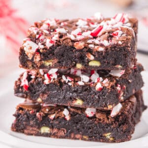 A close up of stacked Candy Cane Brownies showing a fudgy chocolate texture with crushed peppermint pieces and mint baking chips throughout.