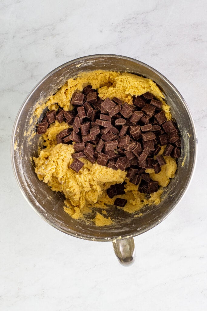 Chocolate chunks sitting on top of the mixed cookie dough, ready to be folded in.