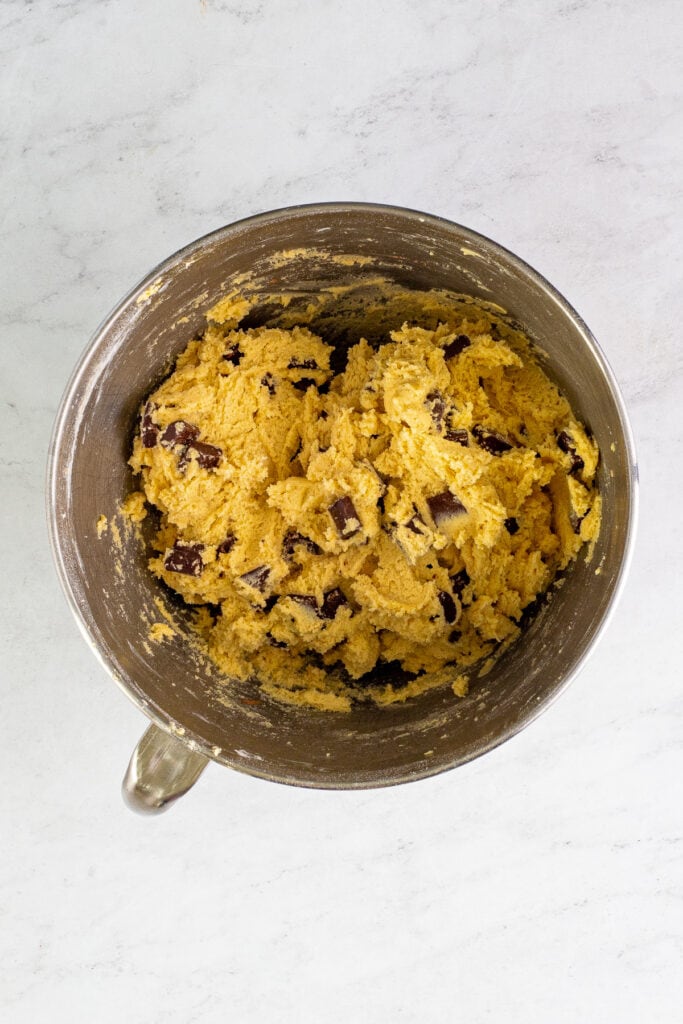 Mixing bowl filled with thick cookie dough with large chocolate chunks throughout, sitting on a light marble surface.