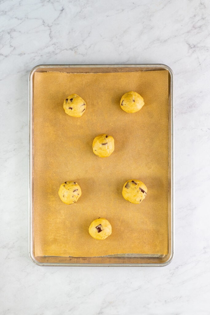 Cookie dough balls arranged evenly on a parchment lined baking sheet before baking.