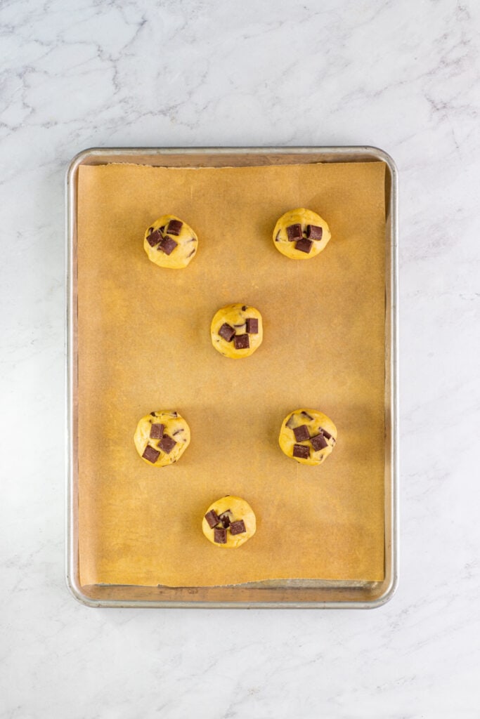 Cookie dough balls topped with extra chocolate chunks placed on a parchment lined sheet pan.