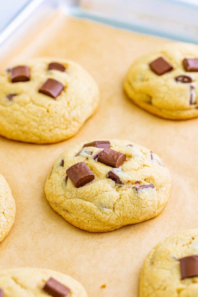 Freshly baked cookies with chocolate chunks on a parchment lined baking sheet.