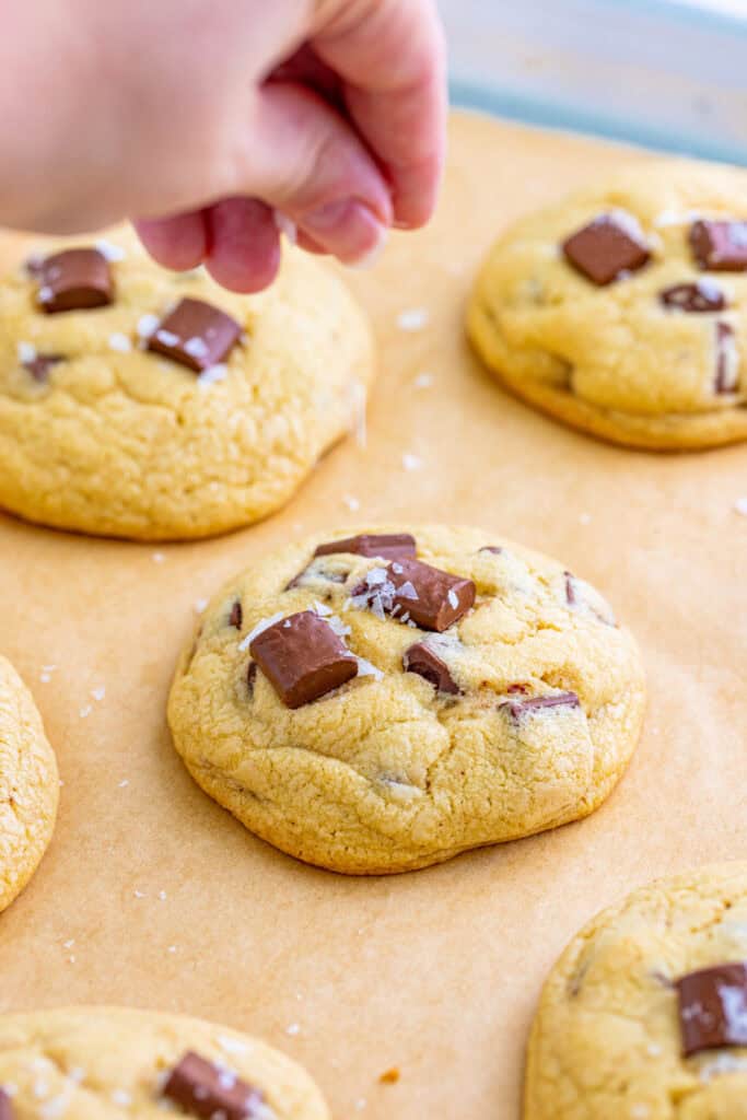 Hand sprinkling flaky sea salt over warm cookies topped with chocolate chunks.