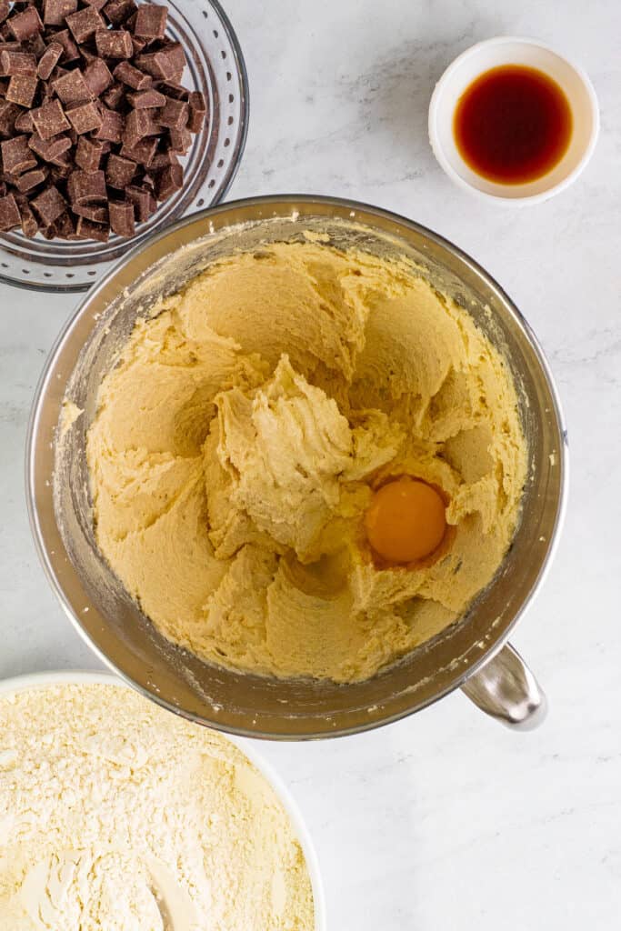 Mixing bowl filled with creamed butter and sugars with a cracked egg added on top before mixing.