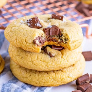 Square cropped image of a bitten cookie stacked on more cookies, showing a soft center and melted chocolate pieces.