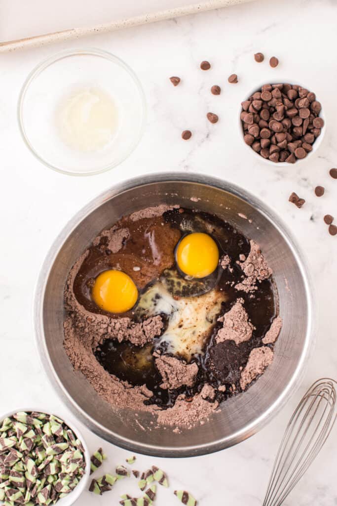 Eggs and melted butter added to the dry ingredients in a mixing bowl for Chocolate Mint Chip Cookies.
