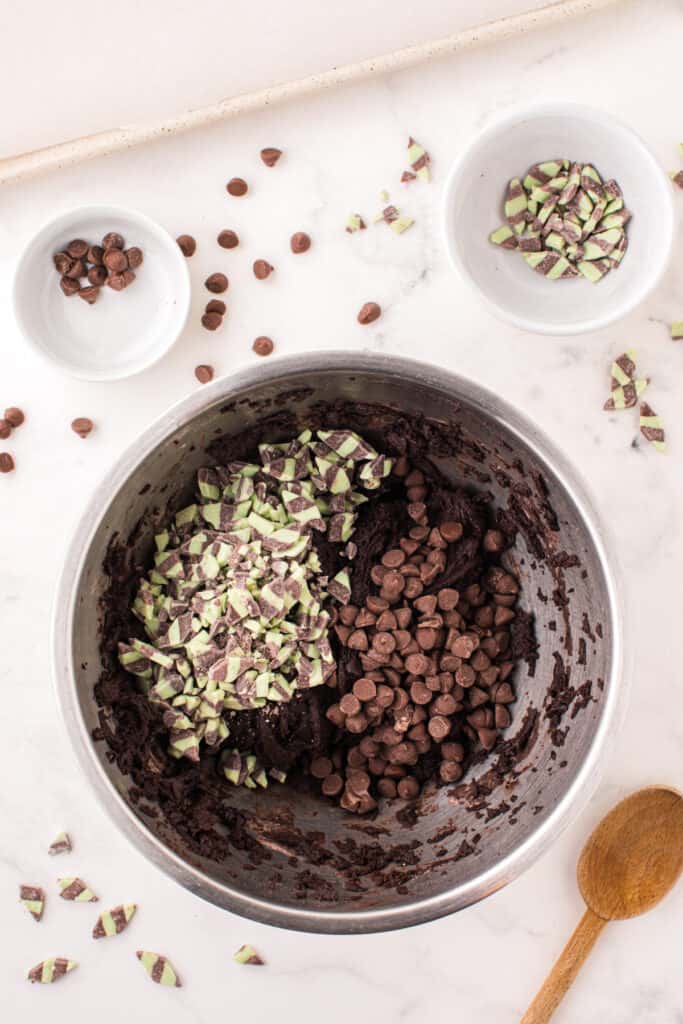 Partially mixed cookie dough in a bowl with mint chips and milk chocolate chips ready to be stirred in.