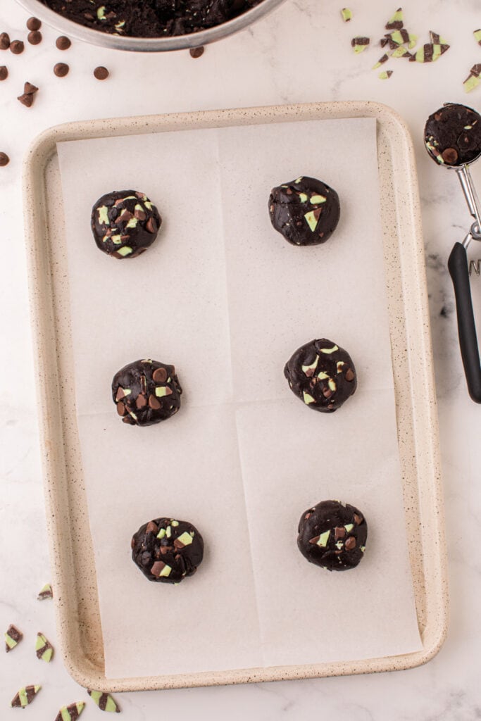 Scooped portions of Chocolate Mint Chip Cookie dough on a parchment-lined baking sheet ready to bake.