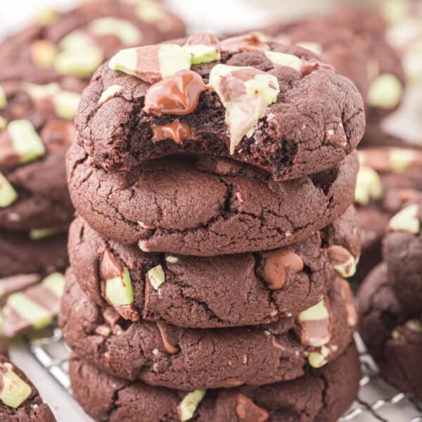 Stack of Chocolate Mint Chip Cookies with the top cookie missing a bite, showing gooey melted chocolate and mint pieces.