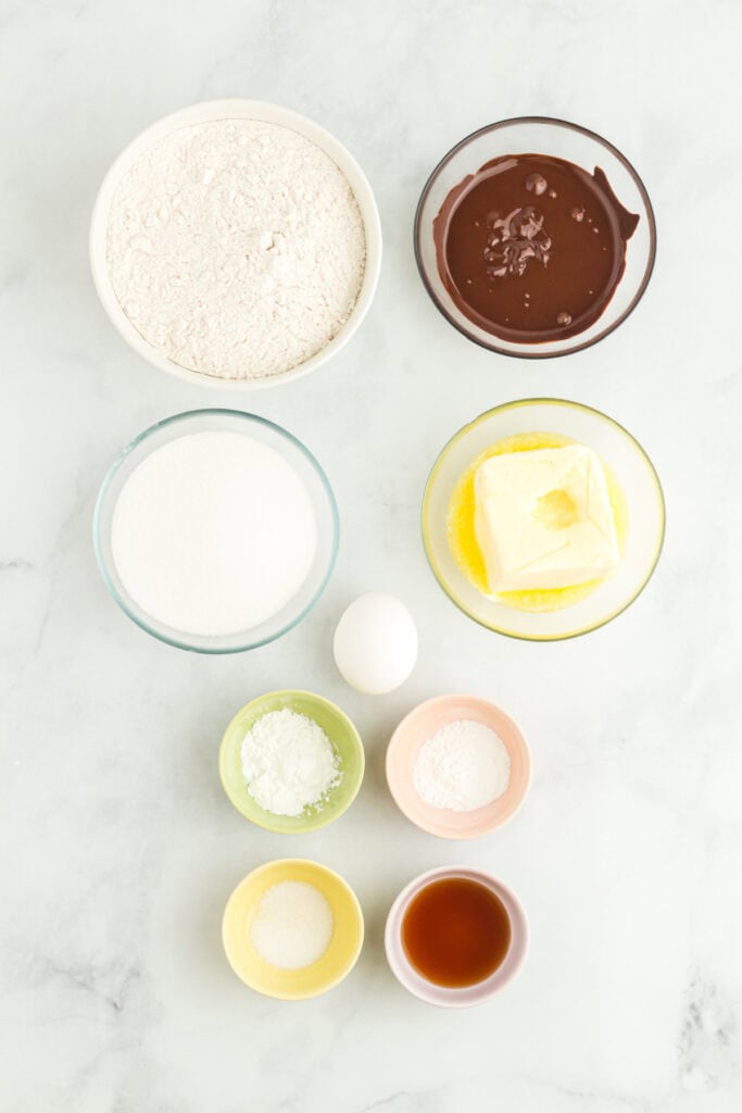 Overhead view of measured ingredients in small bowls, including flour, melted chocolate, sugar, butter, egg, corn starch, baking powder, salt, and vanilla.