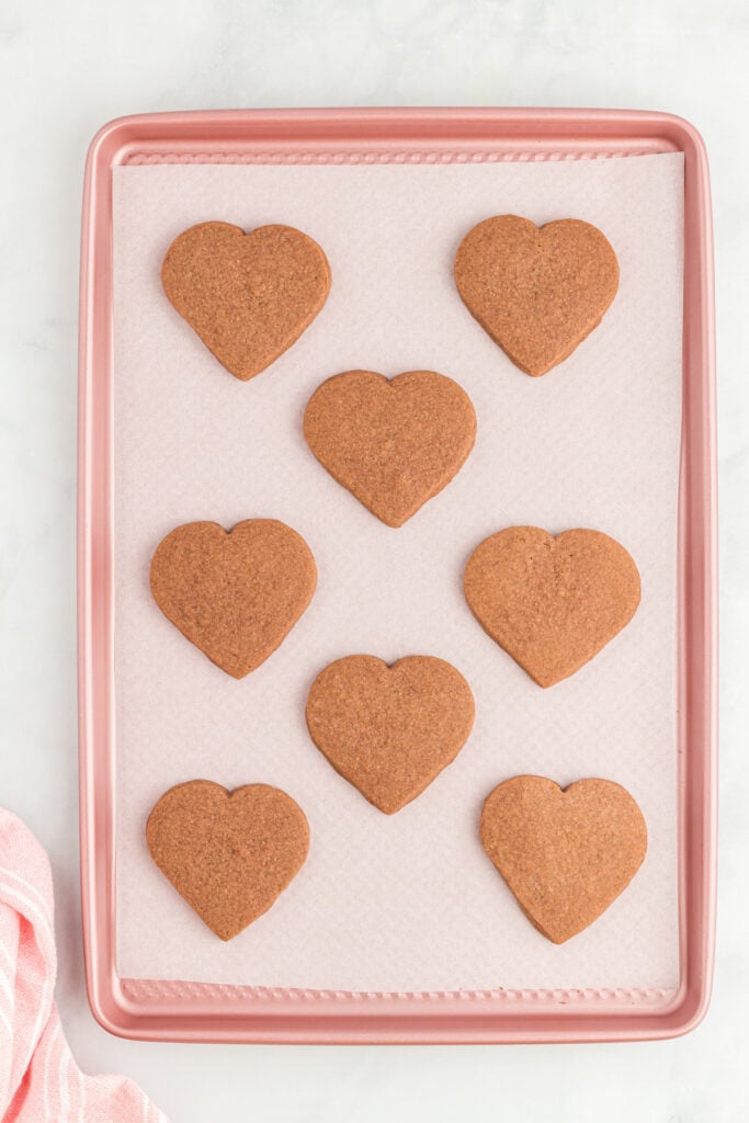 Baked heart shaped chocolate cookies on a parchment lined baking sheet cooling after baking.