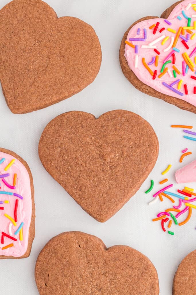 Close view of plain and frosted heart shaped chocolate cookies with colorful sprinkles around them.