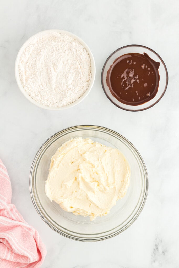 Bowl of creamed butter and sugar next to bowls of flour mixture and melted chocolate, ready to be combined.